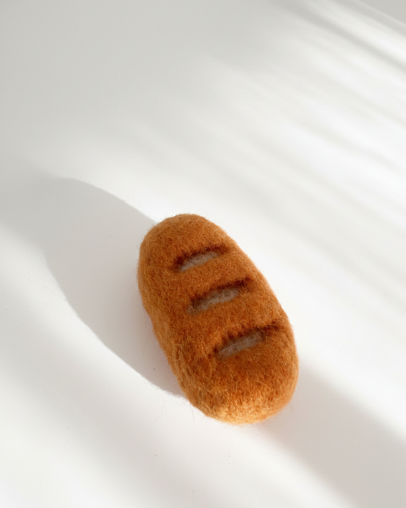 Needle-felted baguette magnet made from natural wool with scored surface detail