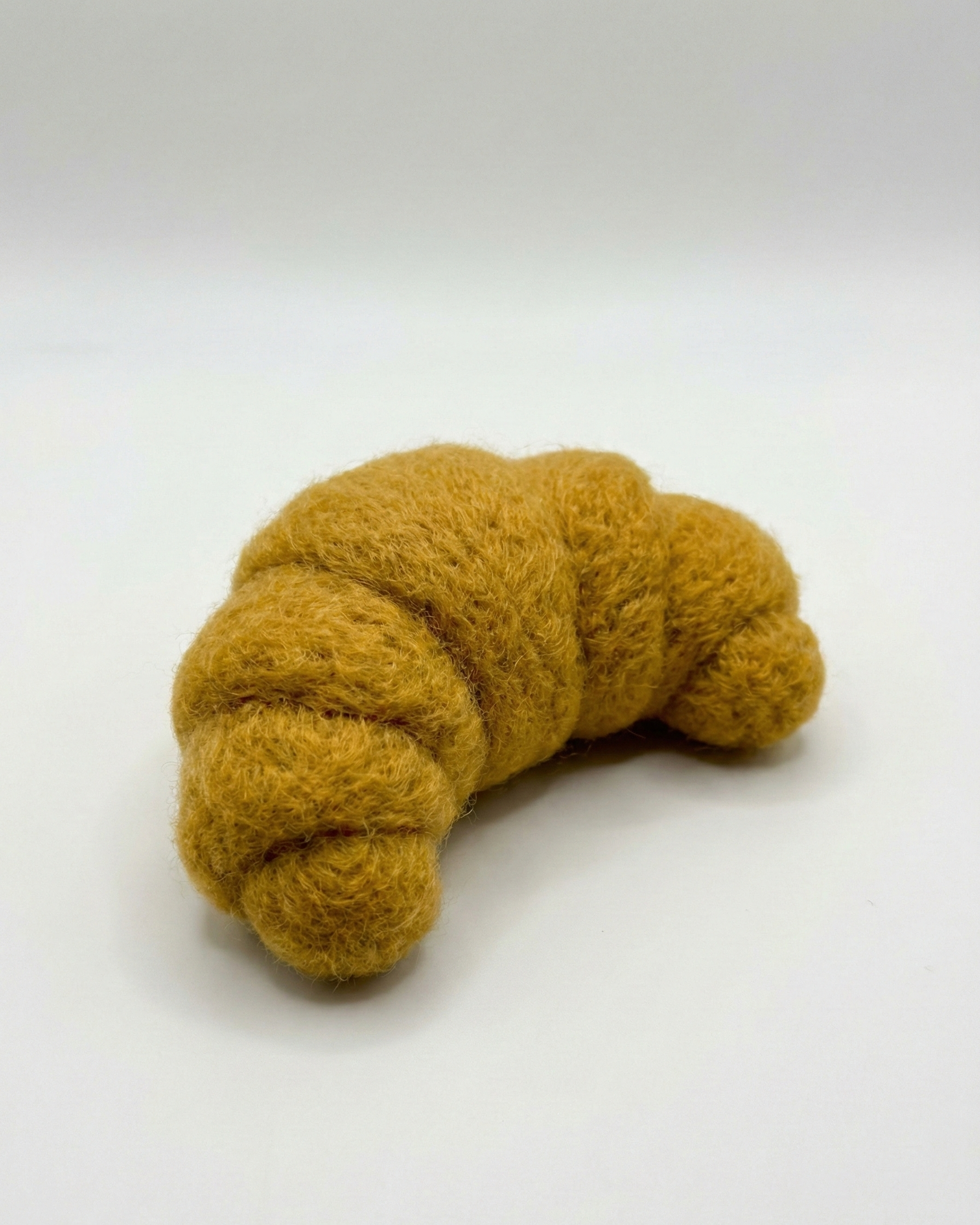 Handmade needle felted croissant magnet in the white background.
