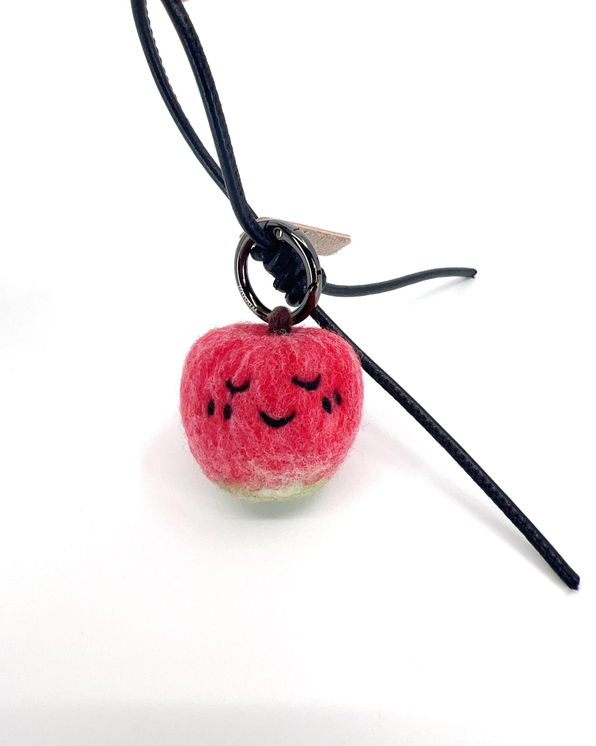 Hanging view of needle-felted wool apple keychain with black leather cord, featuring a hand-stitched happy smiley face.
