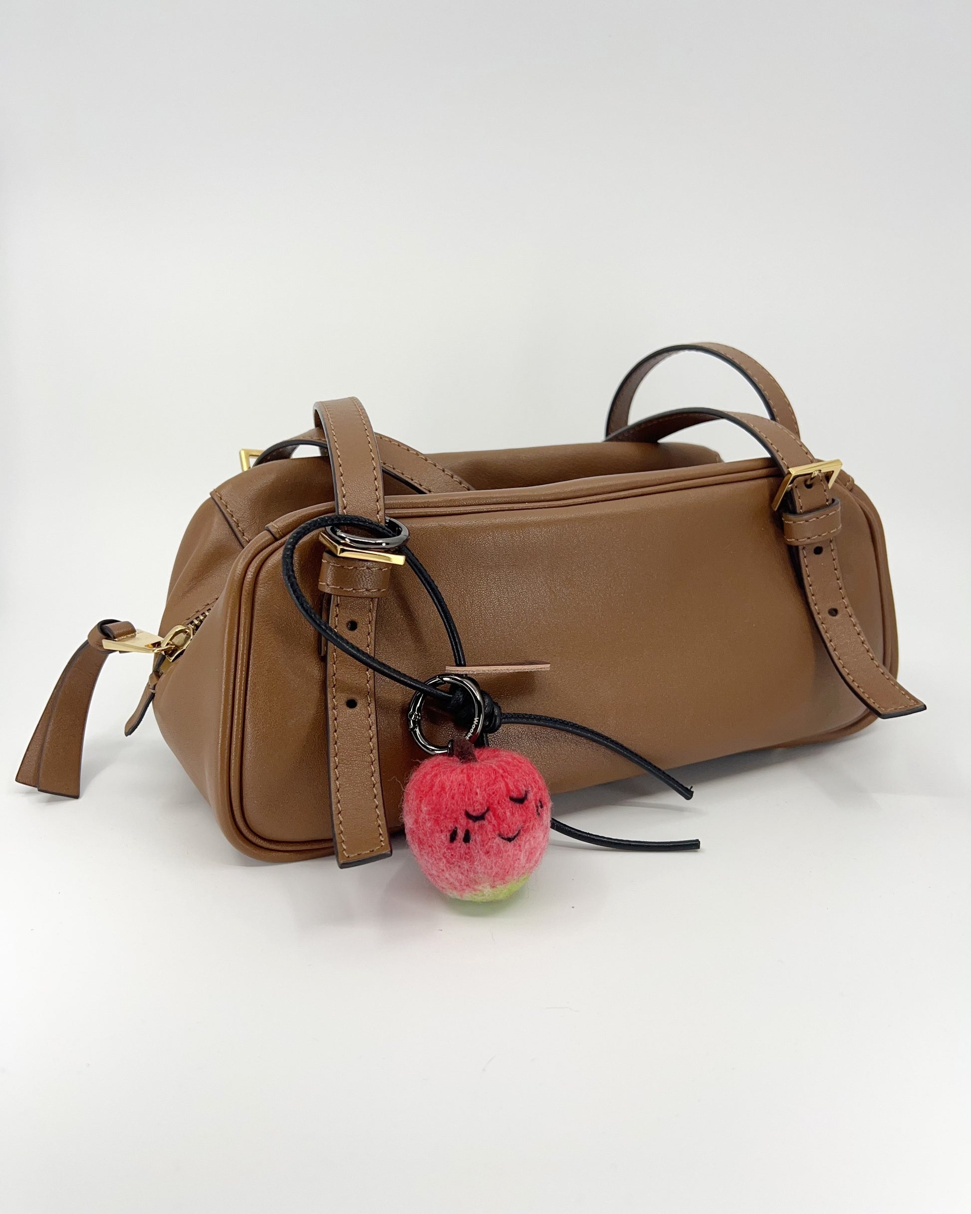 Lifestyle photography of handmade wool apple bag charm clipped onto a brown leather handbag, showing size and styling.