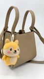 A tan leather mini tote bag shown against a plain white background, featuring a handmade Woobbi fox keychain hanging from the front handle. The fox charm is made of yellow and cream wool felt with pink cheeks and a smiling face. A white tag labeled 'Woobbi' connects the charm to the bag's hardware.