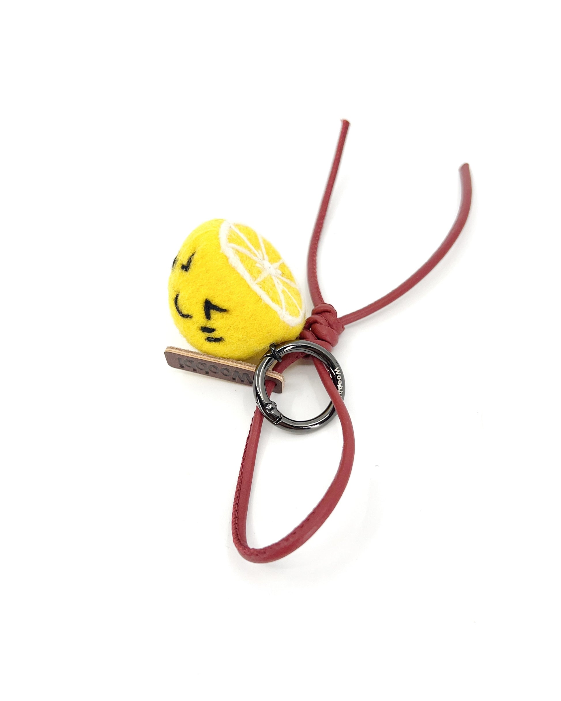 Studio shot of handcrafted wool lemon keychain featuring a red leather loop, black metal hardware, and a cute winking face.