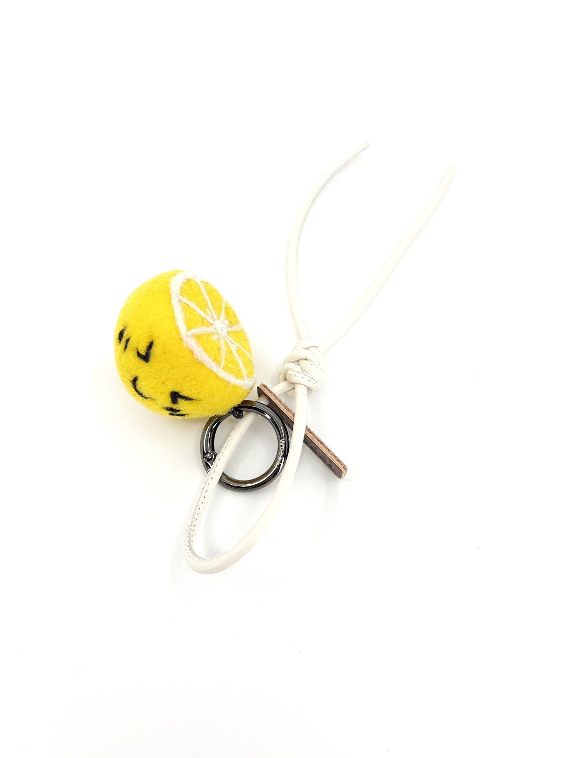 Sustainable citrus bag accessory featuring a yellow needle-felted lemon slice with white leather strap and knot detail.