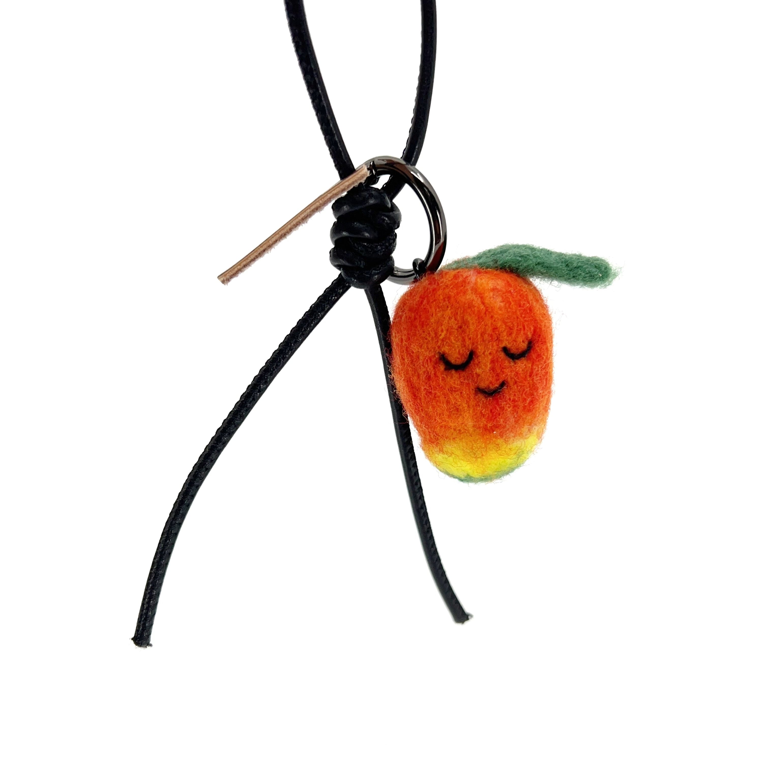 Sustainable needle-felted mango keychain with black leather cord and brown Woobbi brand tag, styled as a tropical bag accessory.
