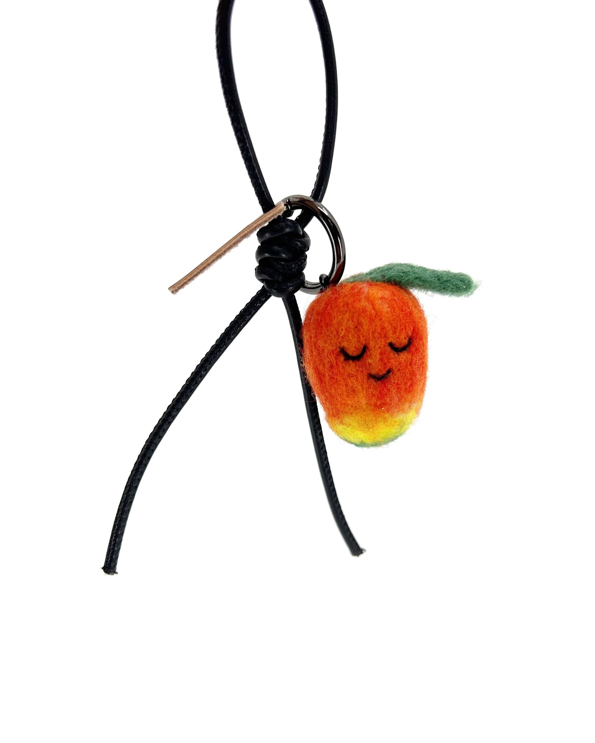 Sustainable needle-felted mango keychain with black leather cord and brown Woobbi brand tag, styled as a tropical bag accessory.