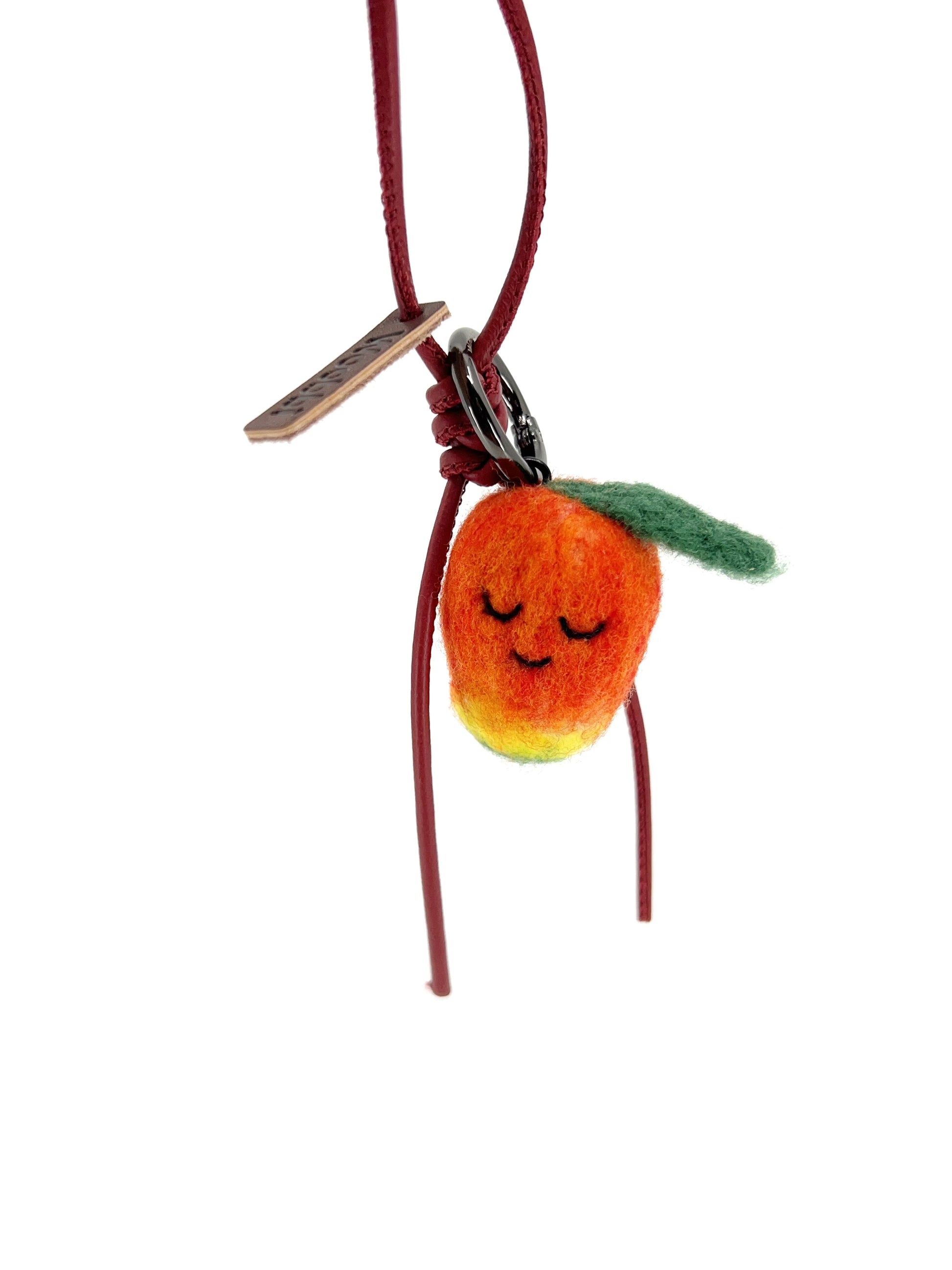 Handcrafted wool mango fruit charm attached to a deep red leather loop with a green leaf detail, isolated on a white background.