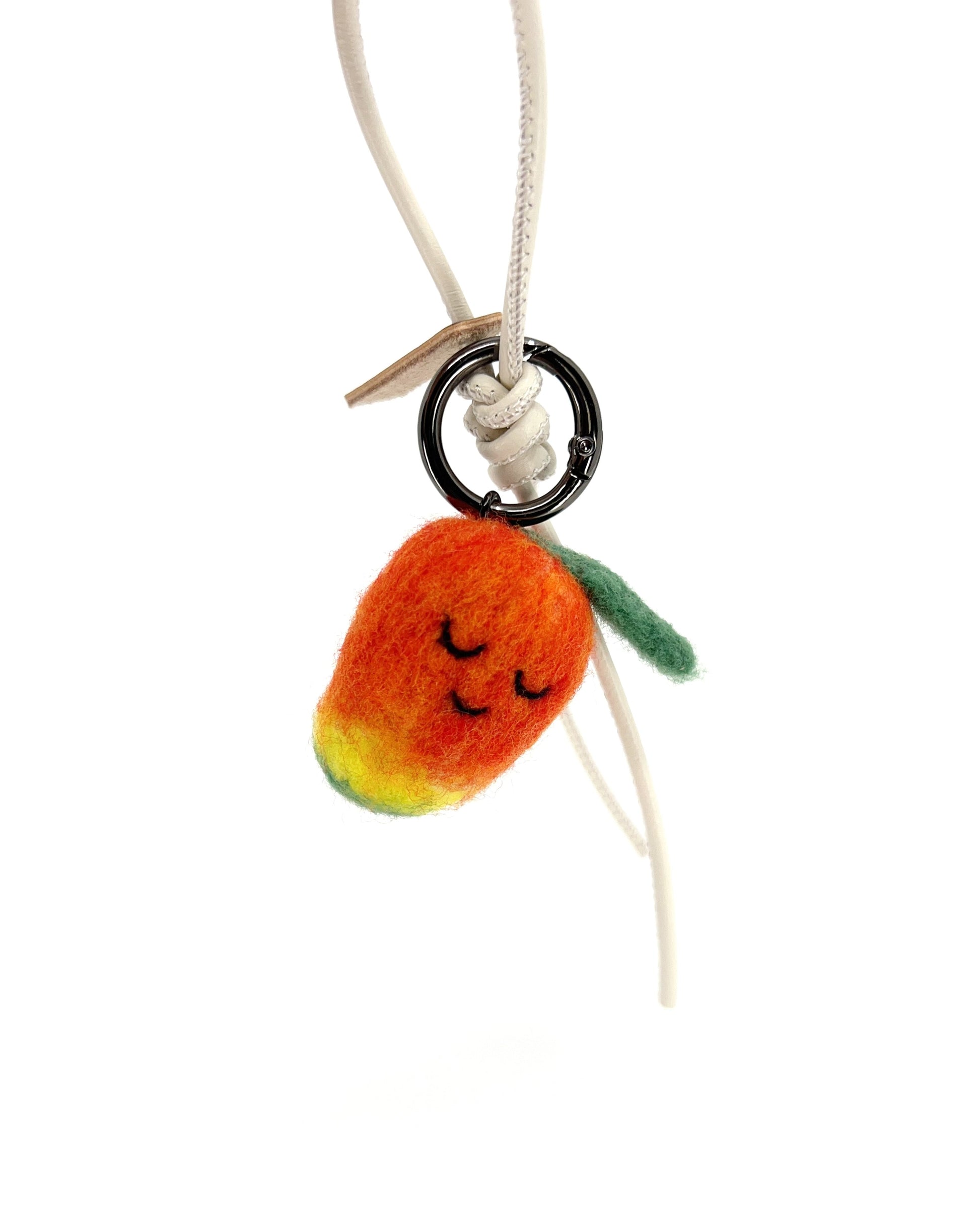Hanging view of needle-felted wool mango bag charm featuring a white leather cord, showing the soft orange-to-yellow gradient and sleeping face.