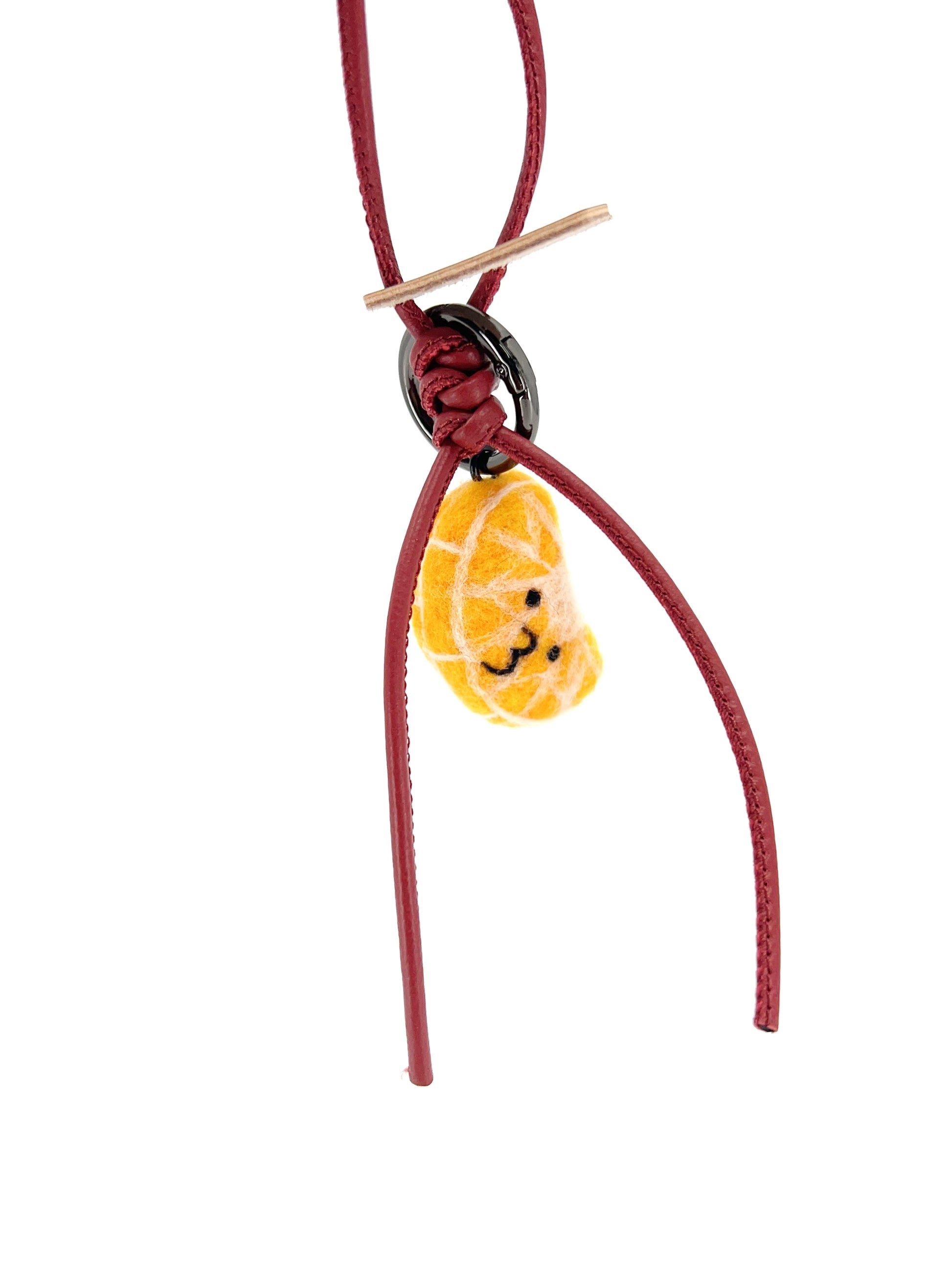 Sustainable needle-felted tangerine bag accessory attached to a red leather loop with knot detail, displayed on a clean white background.