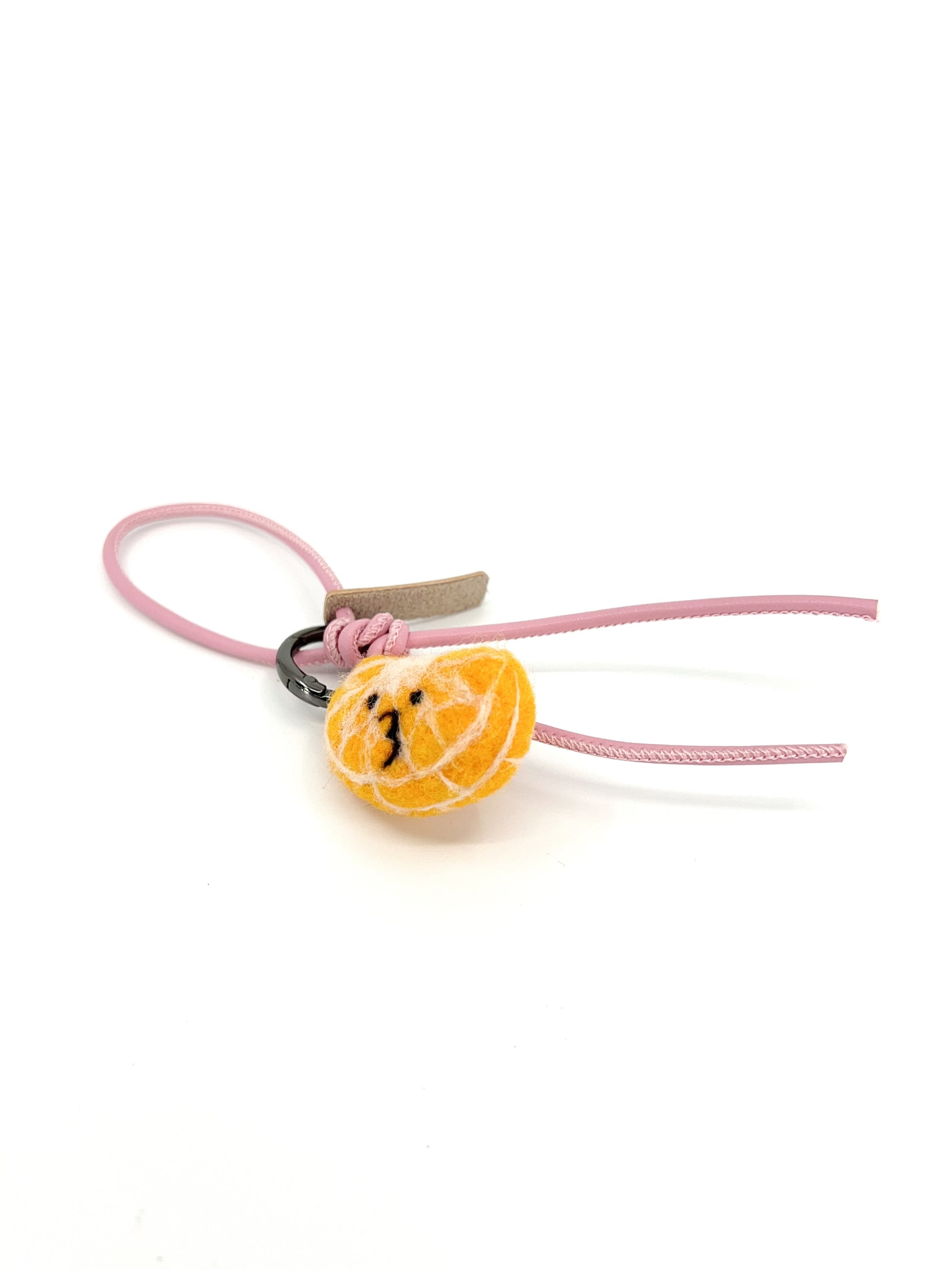 Studio product shot of cute needle-felted mandarin orange slice bag charm with pink leather strap and embroidered smiley face, isolated on white.