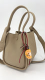 Lifestyle shot of handcrafted needle-felted orange slice bag charm with red leather strap clipped onto a beige leather handbag, showing the cute fruit accessory in use.