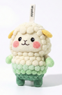 Front view of a handmade Woobbi sheep keychain, crafted from off-white and green bubbly wool felt. It has small yellow ears, rosy pink cheeks, and a smiling face with black eyes and nose. A small tag with the brand name 'Woobbi' is attached to the top. It is set against a plain white background.
