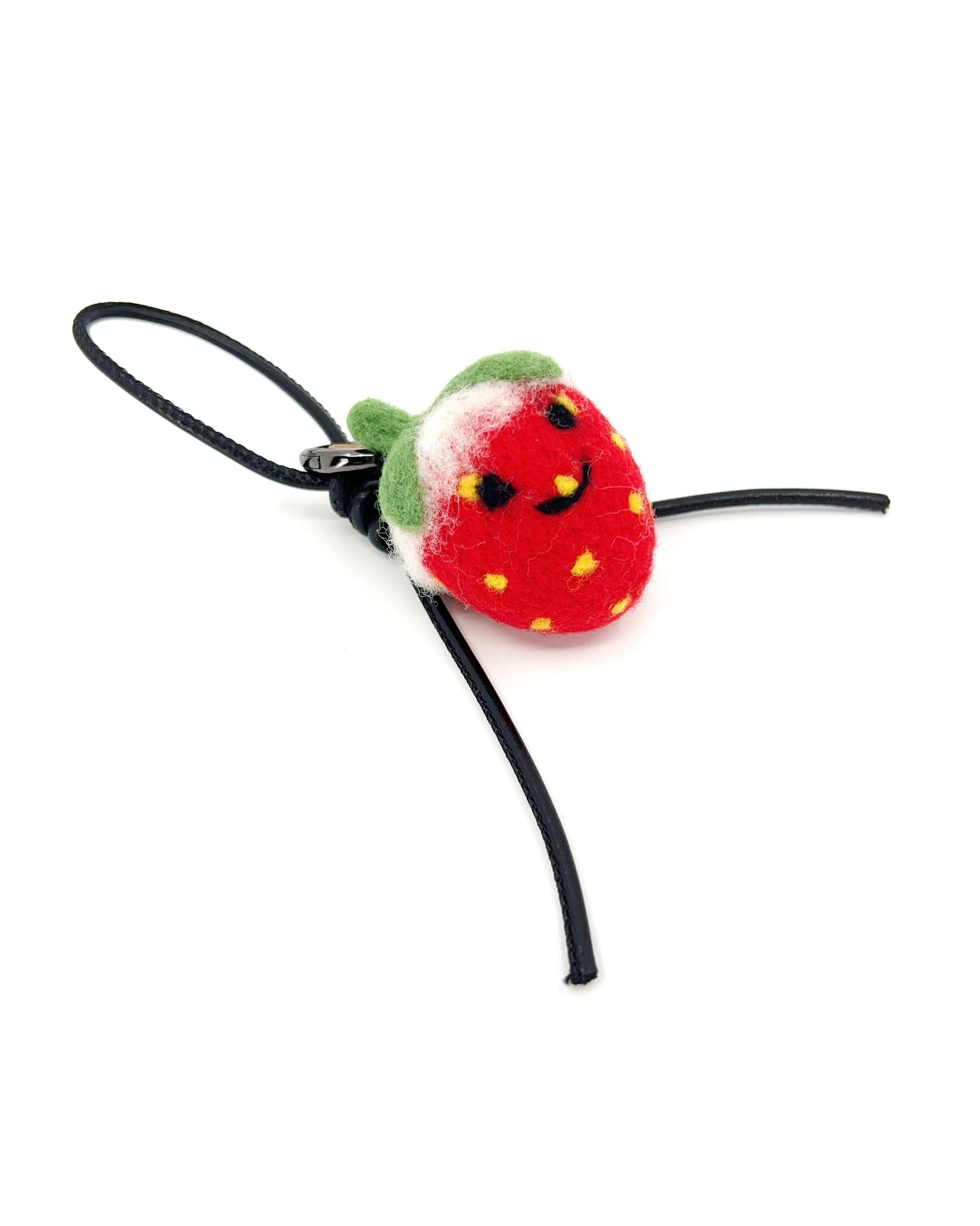 Studio shot of needle-felted wool strawberry bag charm featuring a black leather cord and cute smiley face, isolated on a white background.