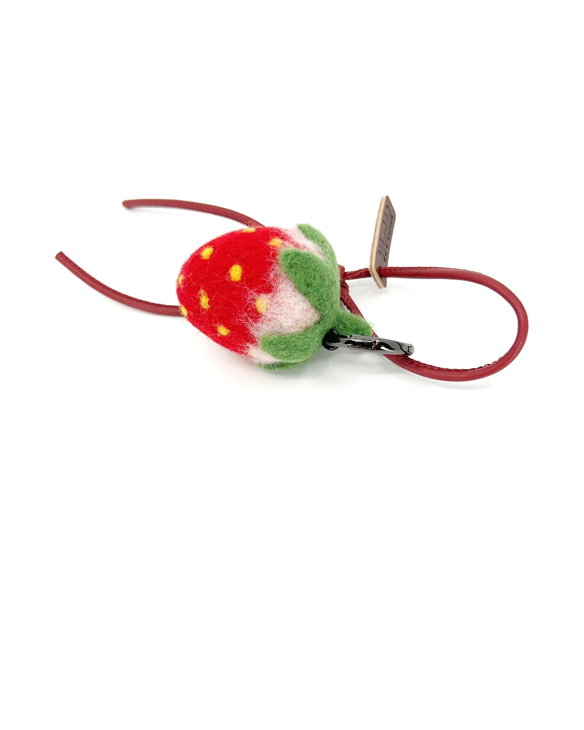 Side view of soft needle-felted strawberry fruit charm attached to a red leather strap with a brown Woobbi brand tag.