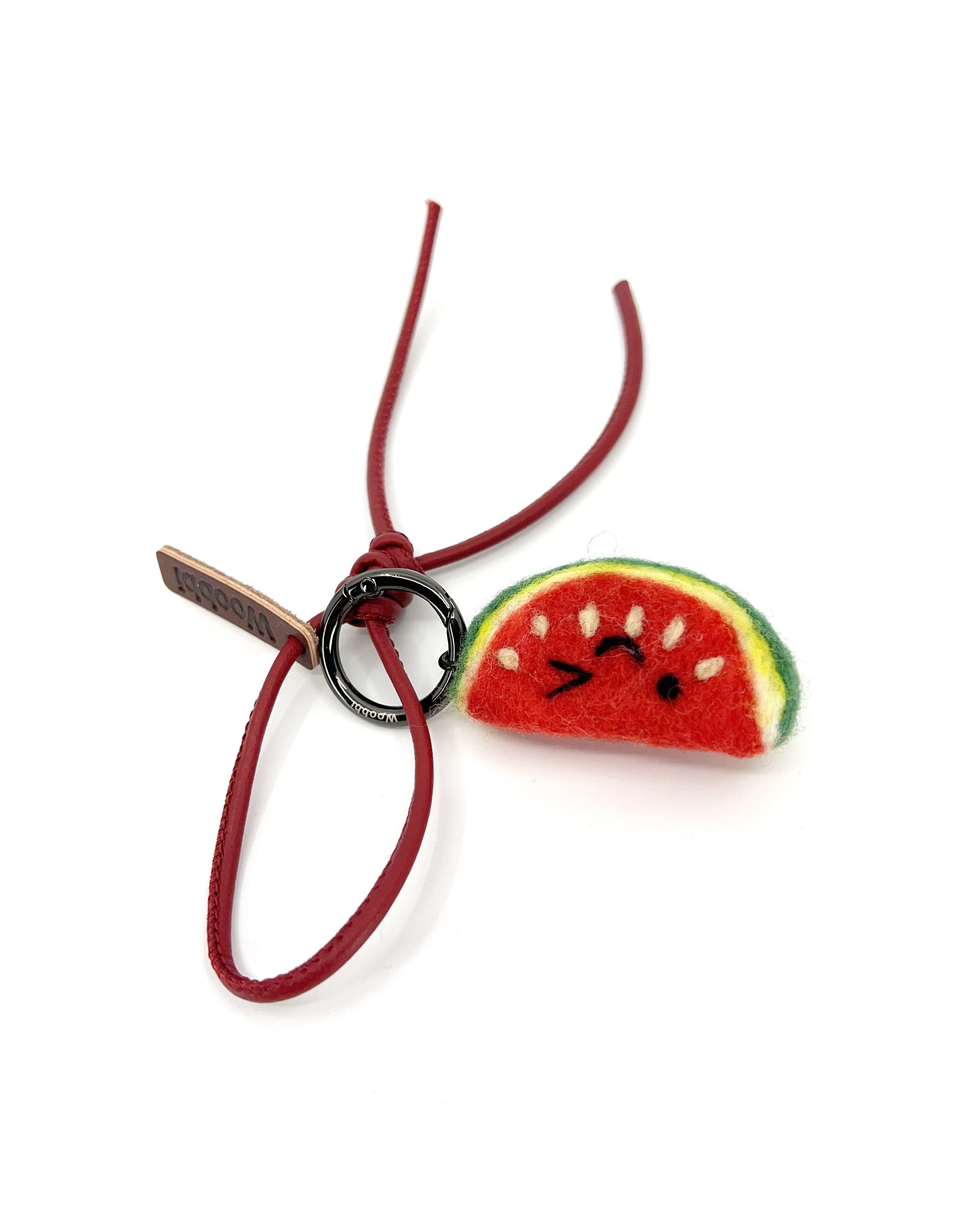 Red needle-felted watermelon fruit charm attached to a matching red leather strap with knotted detail, designed as a sustainable bag accessory.