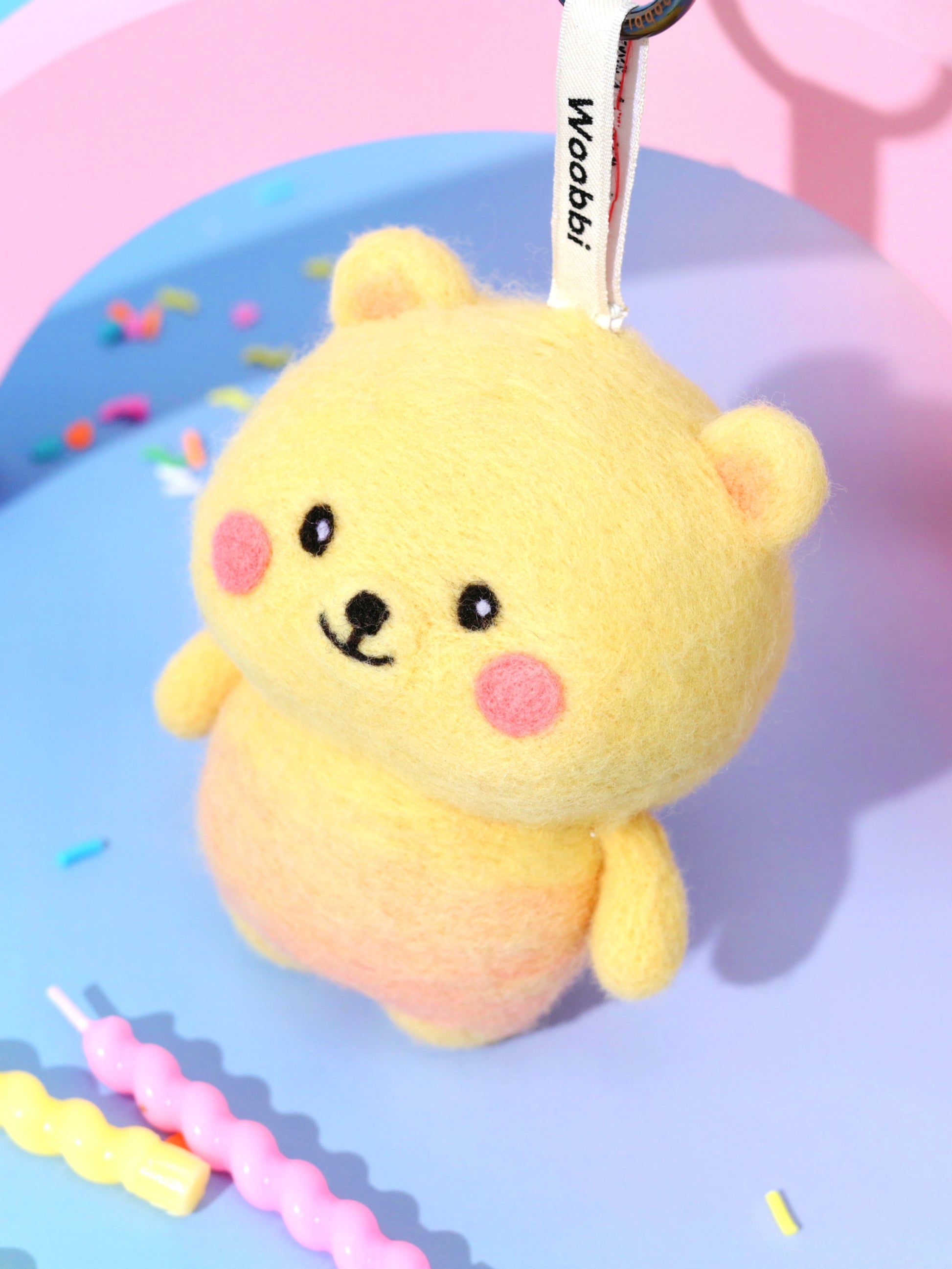 High-angle view of round, chubby wool bear bag charm in yellow and peach, displaying its soft needle-felted shape and secure keychain attachment.