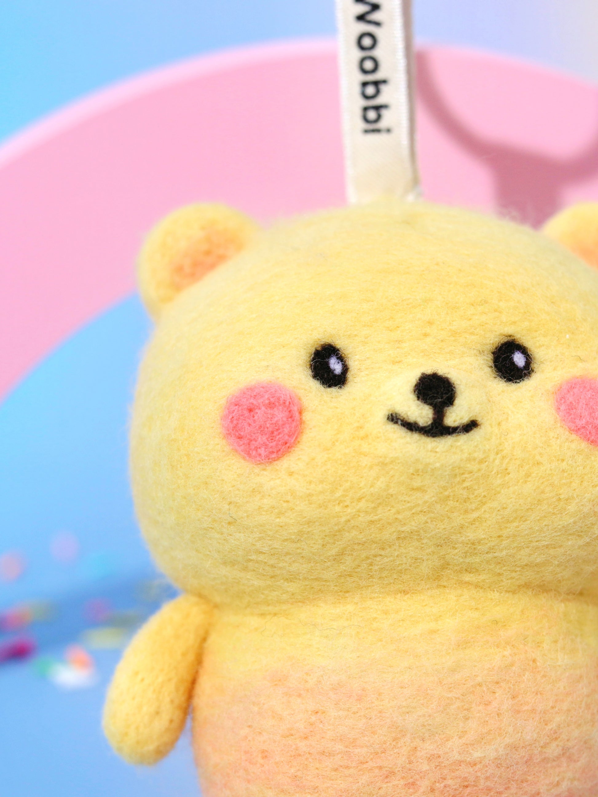 Macro close-up of needle-felted bear face showing the fuzzy Merino wool texture, hand-stitched smile, and rosy pink cheeks.