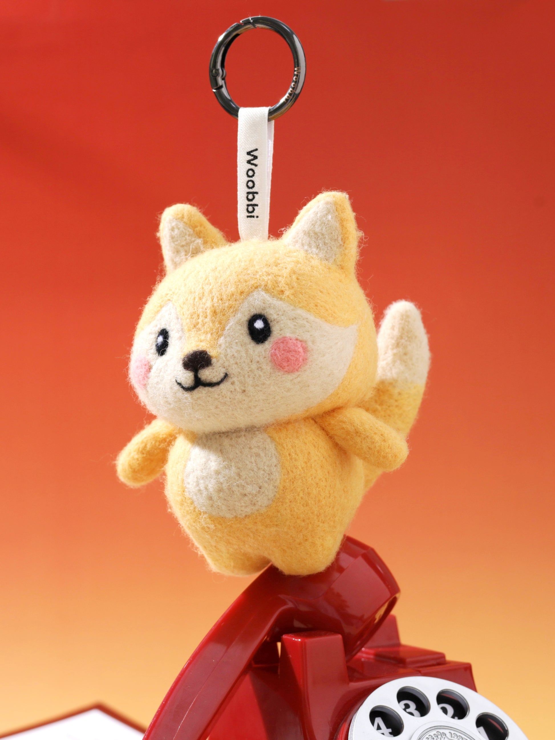 Cute wool fox keychain balancing on a retro telephone receiver, showcasing its sturdy needle-felted structure and playful design.