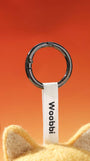 Close-up of durable black metal keychain ring and white woven Woobbi brand tag attached to a wool bag charm.