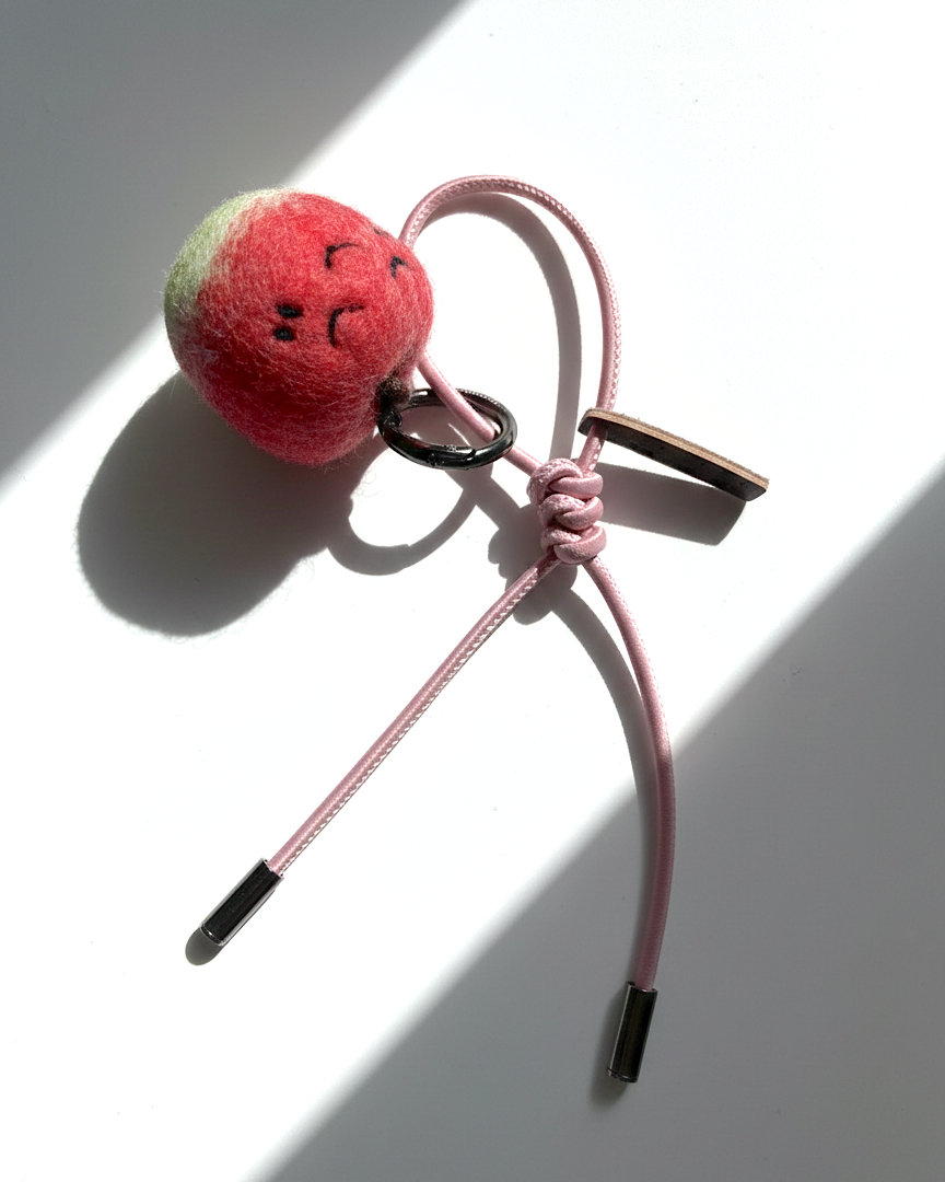 Hanging view of needle-felted wool apple keychain with pink leather cord, featuring a hand-stitched happy smiley face.