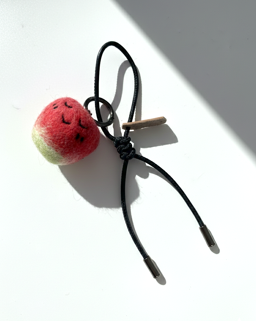 Hanging view of needle-felted wool apple keychain with black leather cord, featuring a hand-stitched happy smiley face.