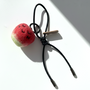 Hanging view of needle-felted wool apple keychain with black leather cord, featuring a hand-stitched happy smiley face.