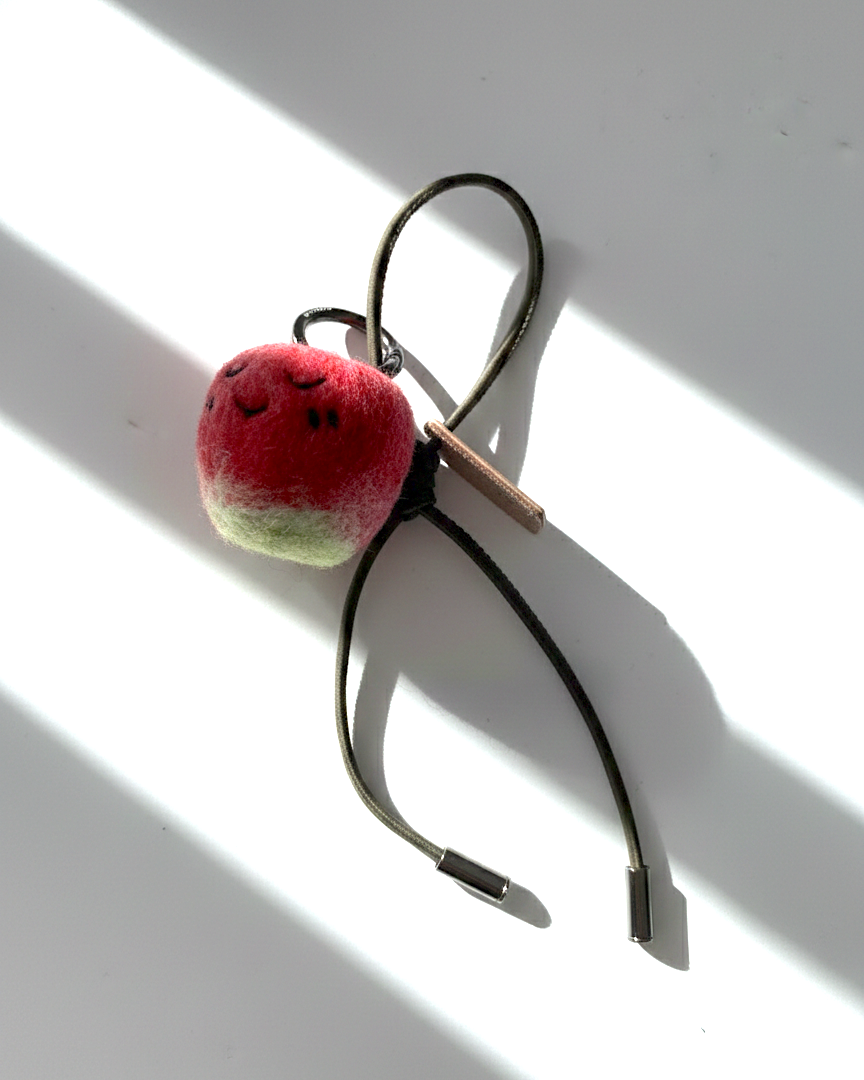 Hanging view of needle-felted wool apple keychain with olive leather cord, featuring a hand-stitched happy smiley face.