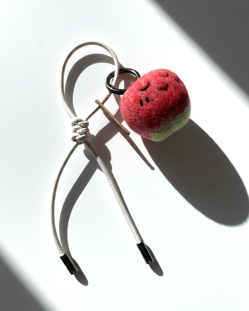 Hanging view of needle-felted wool apple keychain with white leather cord, featuring a hand-stitched happy smiley face.