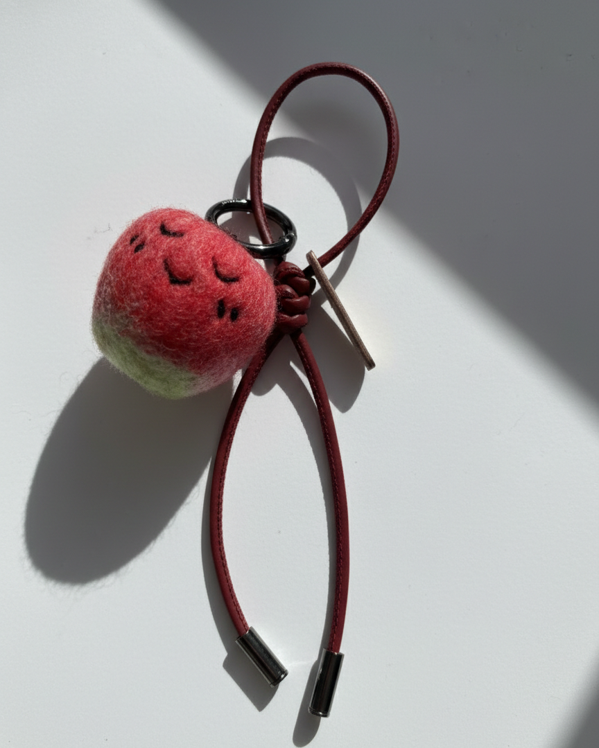 Hanging view of needle-felted wool apple keychain with red leather cord, featuring a hand-stitched happy smiley face.