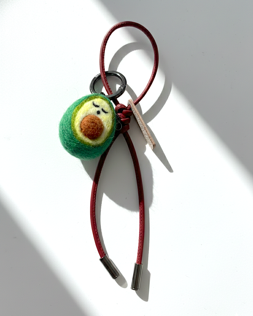 Miniature needle-felted avocado plush charm with dark red burgundy leather cord.