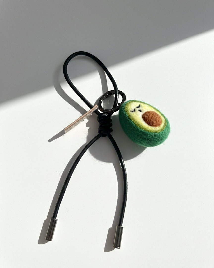 Handcrafted avocado felt charm with black leather cord and polished metal tips.
