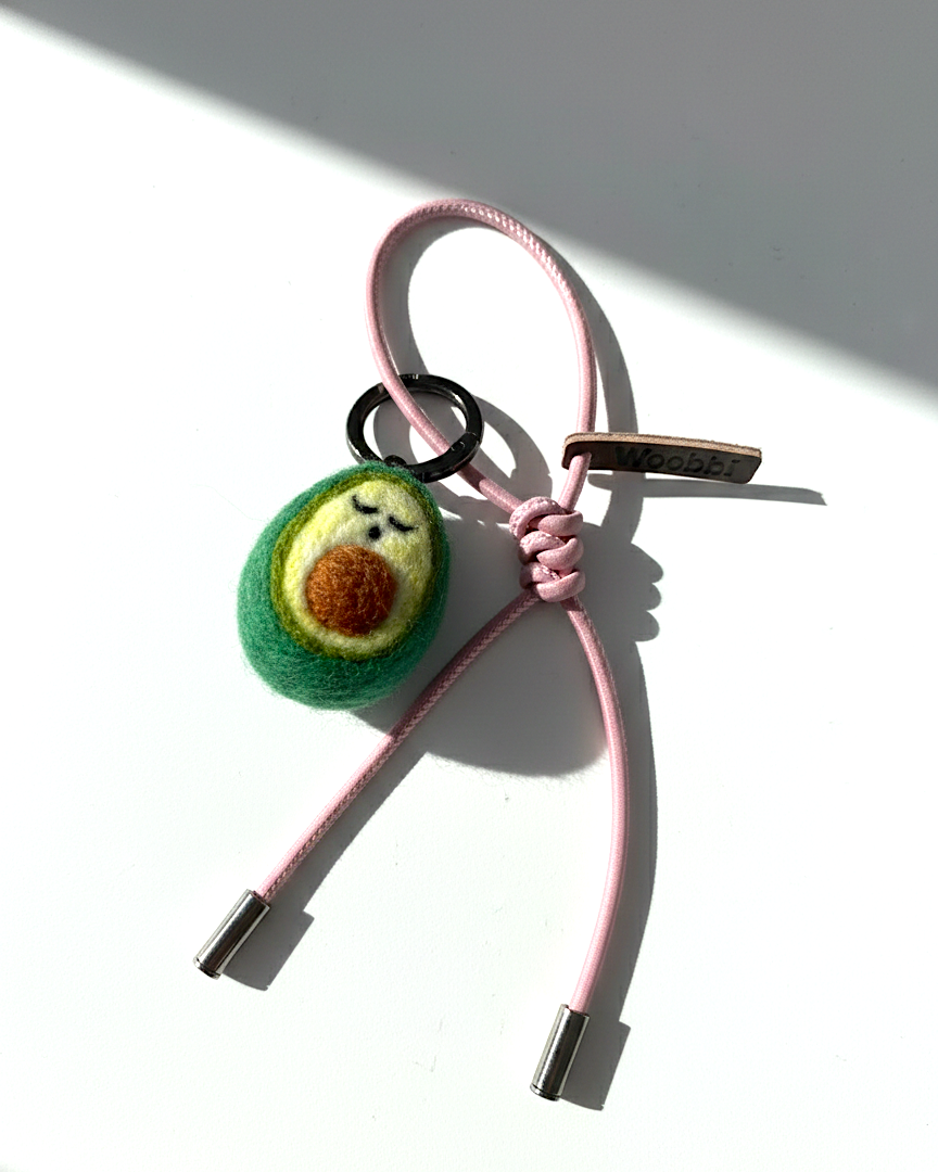 Cute needle-felted avocado accessory with light pink cord and Woobbi brand leather tag.