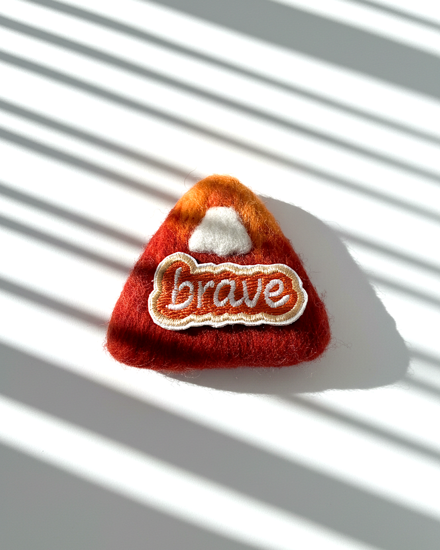 Handmade wool fridge magnet in rust red tones with embroidered Brave patch, needle-felted merino wool