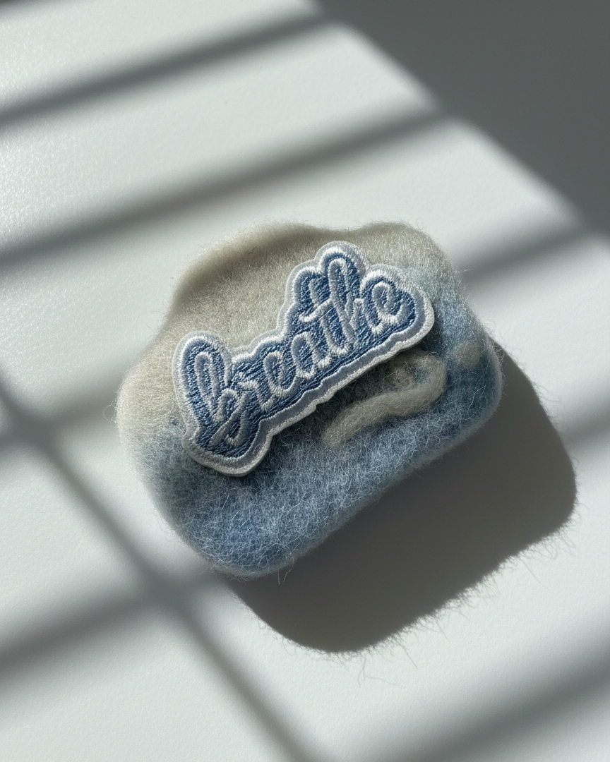 Handmade wool fridge magnet in soft blue and cream tones with embroidered Breathe patch, needle-felted merino wool