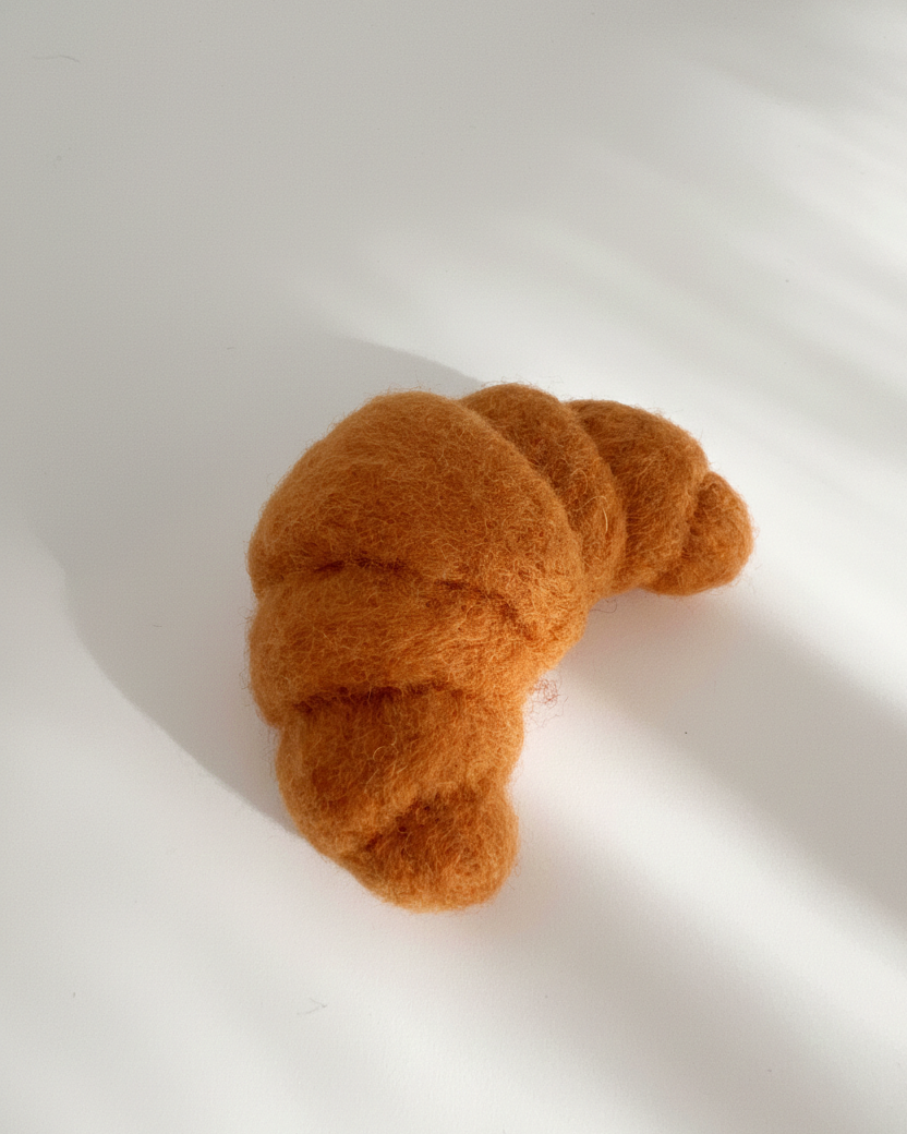 Handmade wool croissant fridge magnet, needle-felted with soft texture and warm golden tones