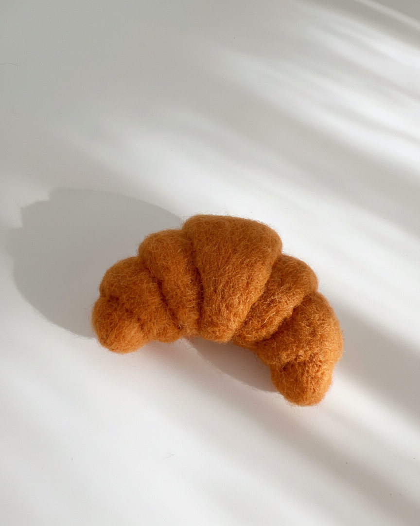 Side view of handmade wool croissant fridge magnet highlighting layered felt folds