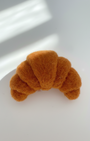 Handmade wool croissant magnet centered on white background with rounded felt shape