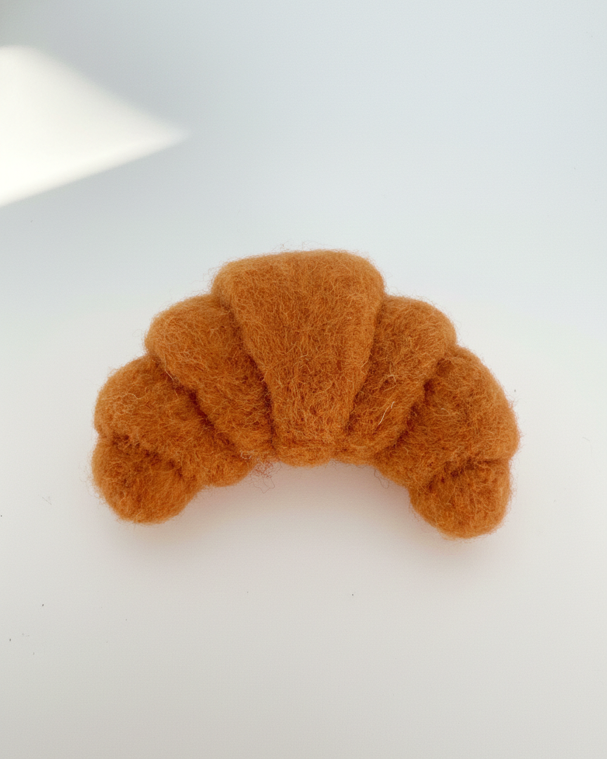 Top-down view of needle-felted wool croissant fridge magnet showing curved form