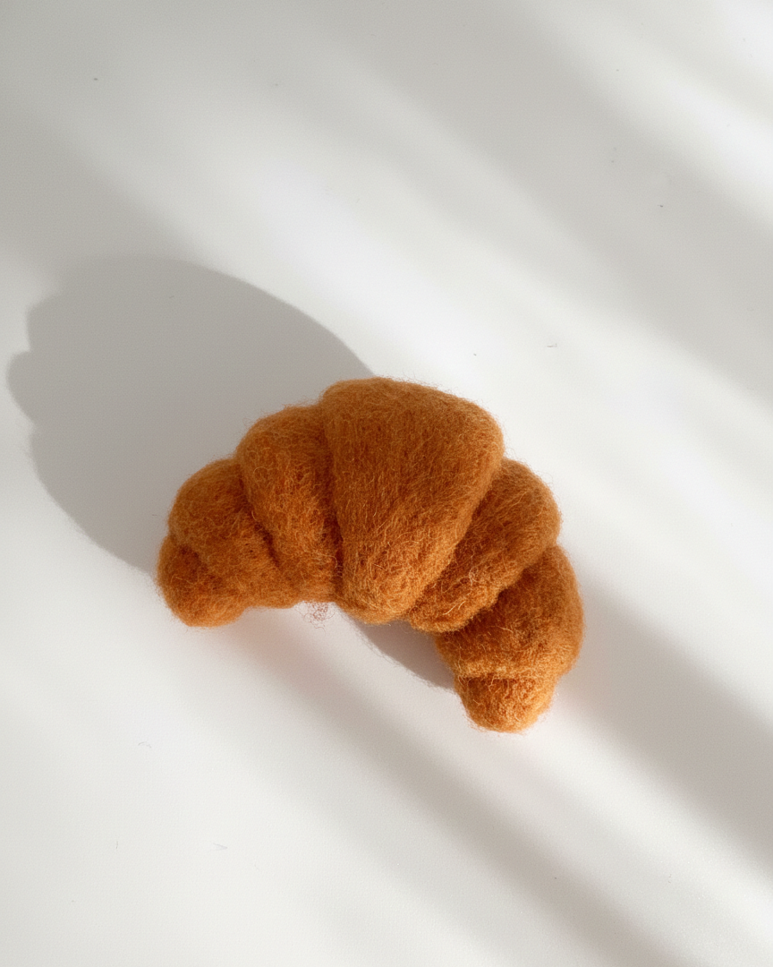 Close-up of handmade wool croissant magnet showing dense felt texture and details