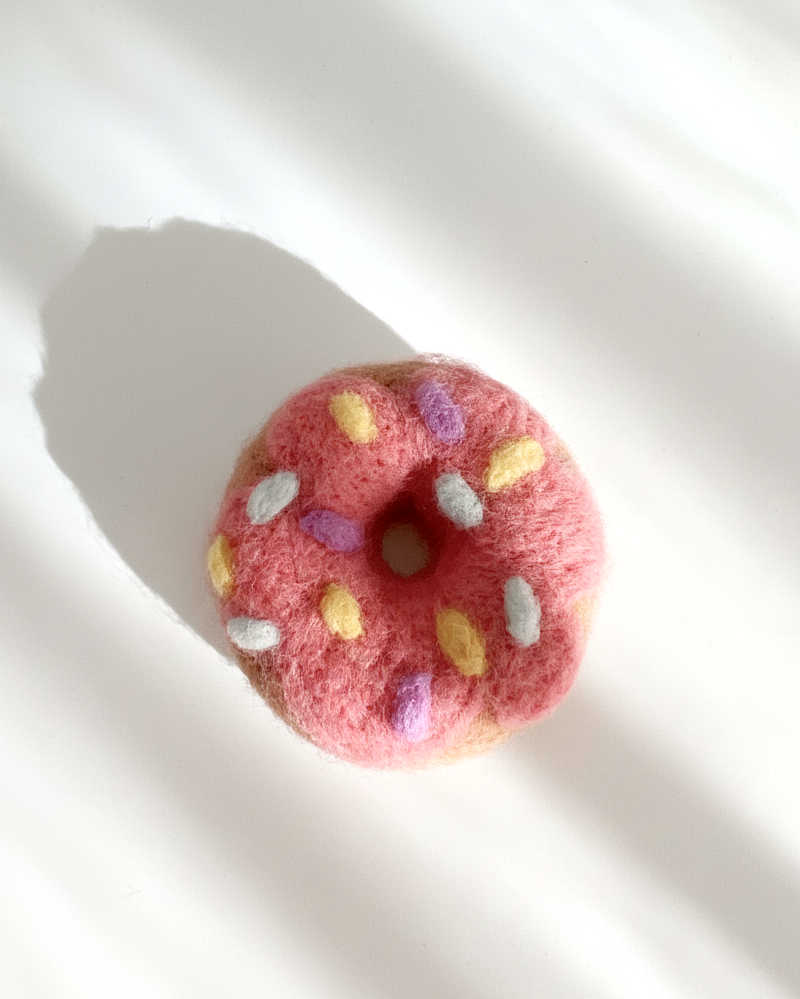 Pink donut-shaped object with colorful sprinkles on a white background