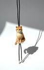 Handmade realistic ginger wool cat sculpture charm in sitting pose, with black sheep skin cord, front view, needle-felted with lifelike details