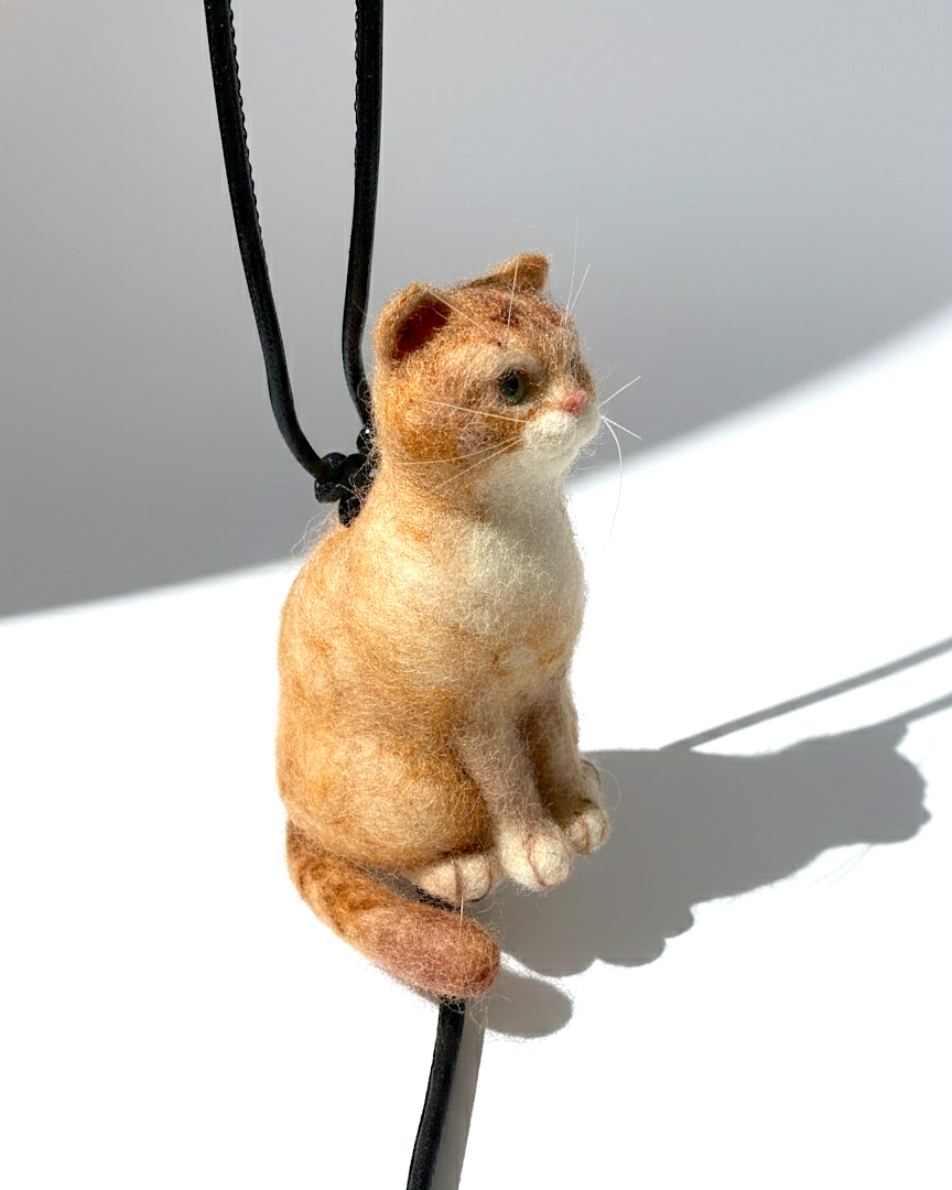 Handmade realistic ginger wool cat sculpture charm in sitting pose, left-side view, needle-felted with lifelike details