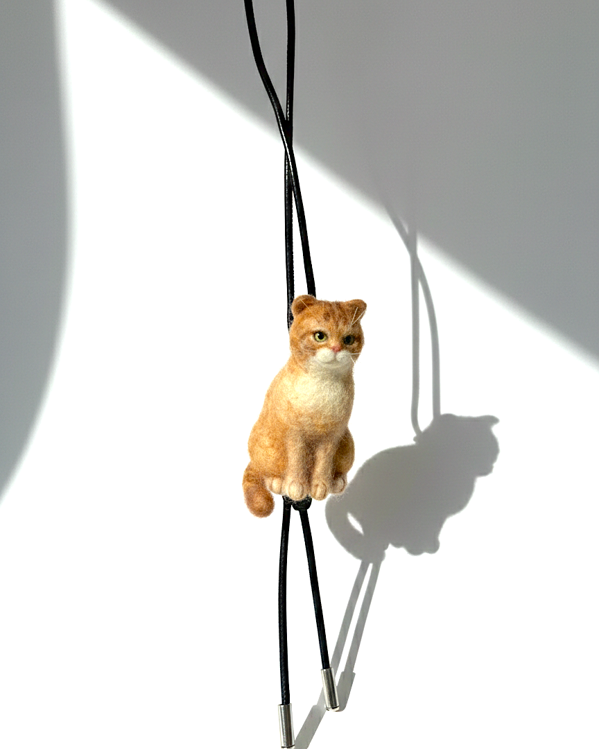 Cat-shaped pendant on a black cord against a white background