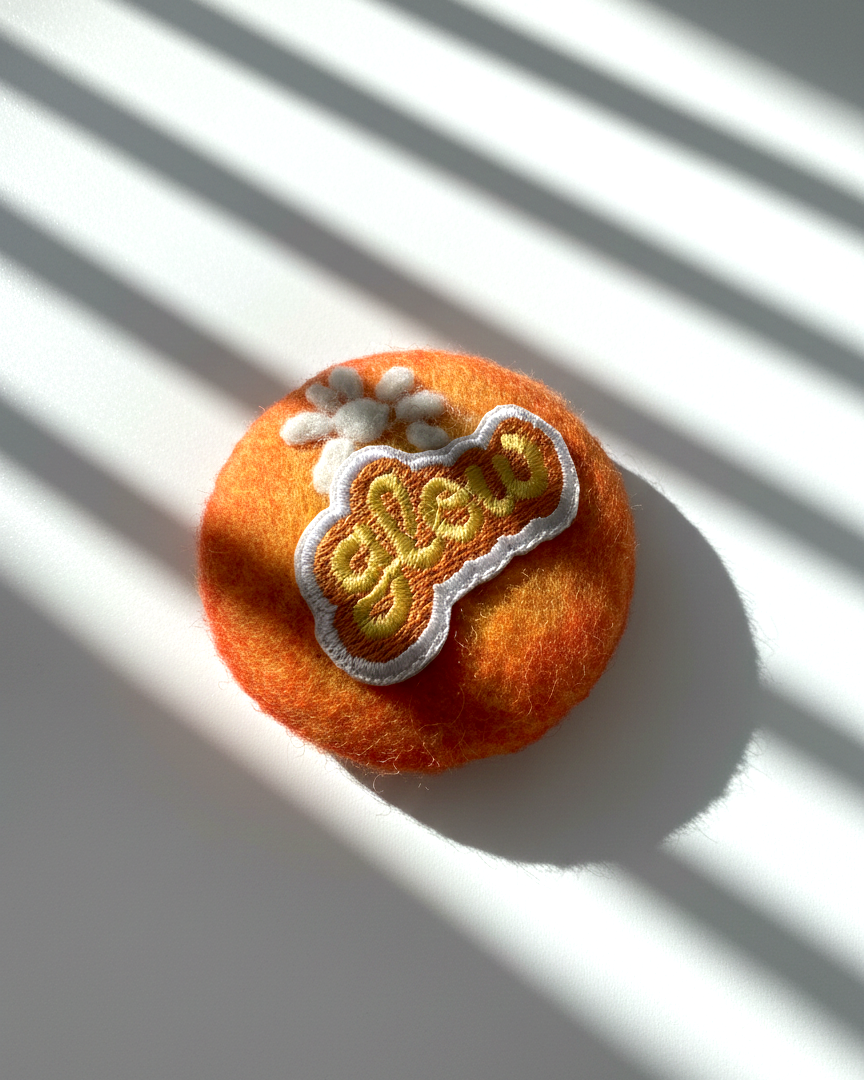 Orange needle-felted wool magnet with stitched Glow patch, soft rounded handmade fridge decor