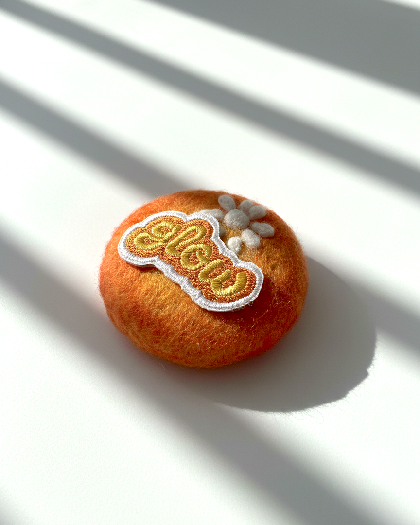 Handcrafted merino wool fridge magnet in warm orange tones featuring Glow embroidery patch