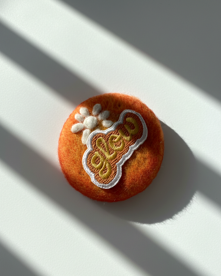 Minimalist orange wool fridge magnet with Glow patch and floral accent, handmade felt home decor