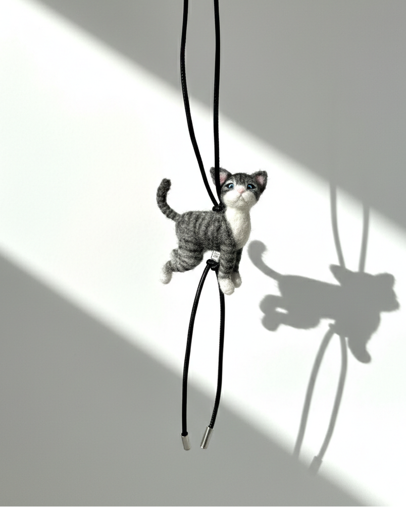 Full view of handmade realistic gray tabby cat wool sculpture charm hanging from black leather strap