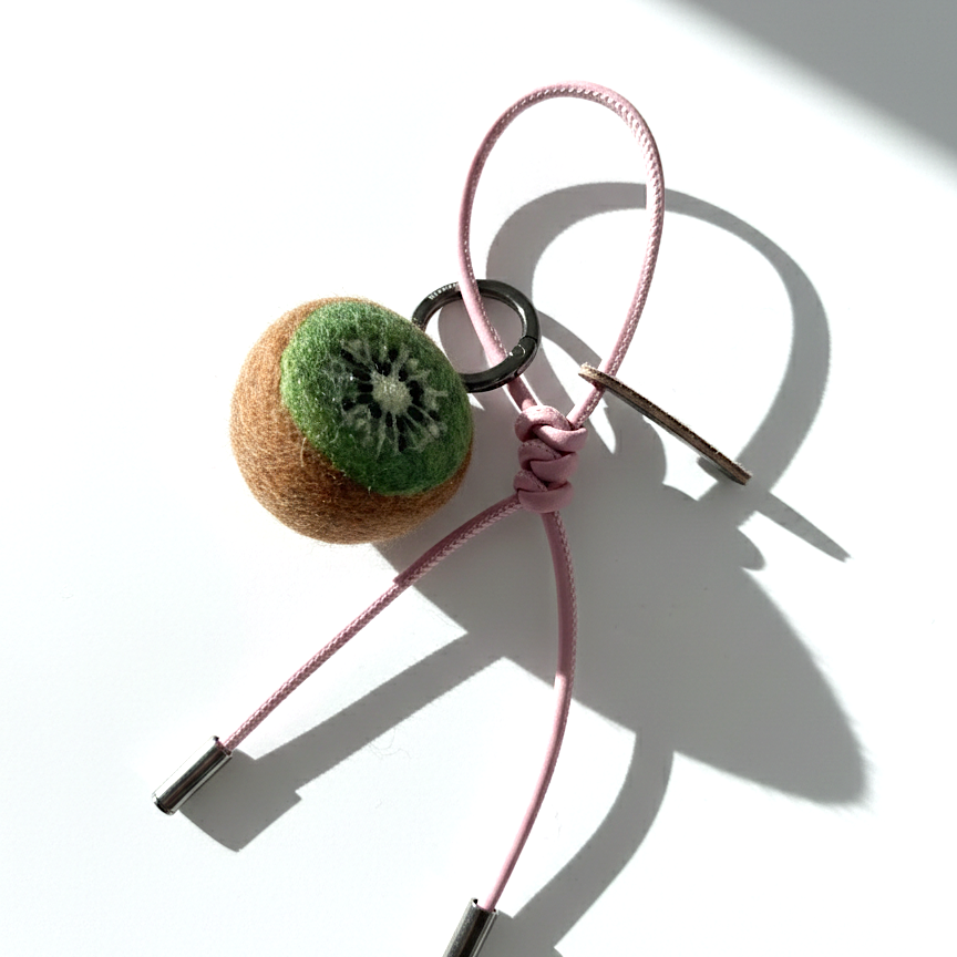 Handmade needle-felted kiwi slice bag charm with a light pink cord and silver hardware.
