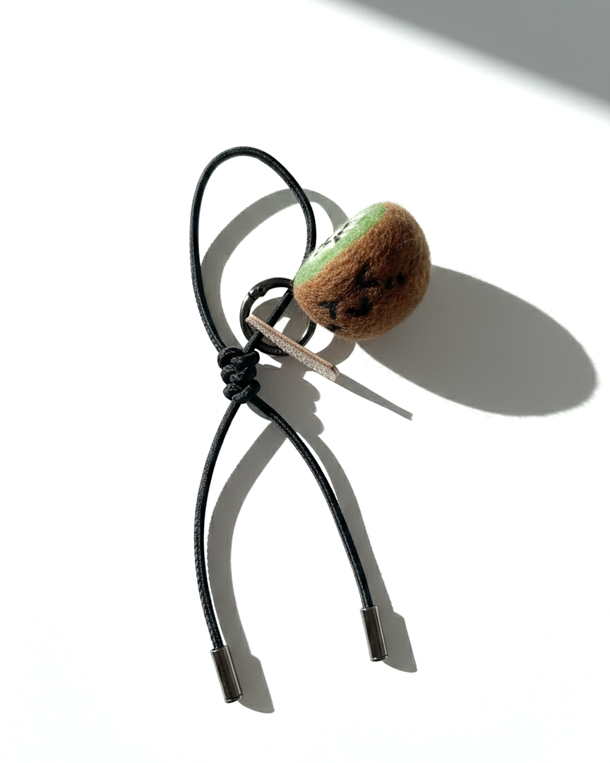 Cute needle-felted kiwi fruit keychain accessory with a black leather cord and metal aglets.