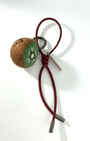 Miniature felted kiwi fruit accessory featuring a dark red leather cord and polished metal tips.