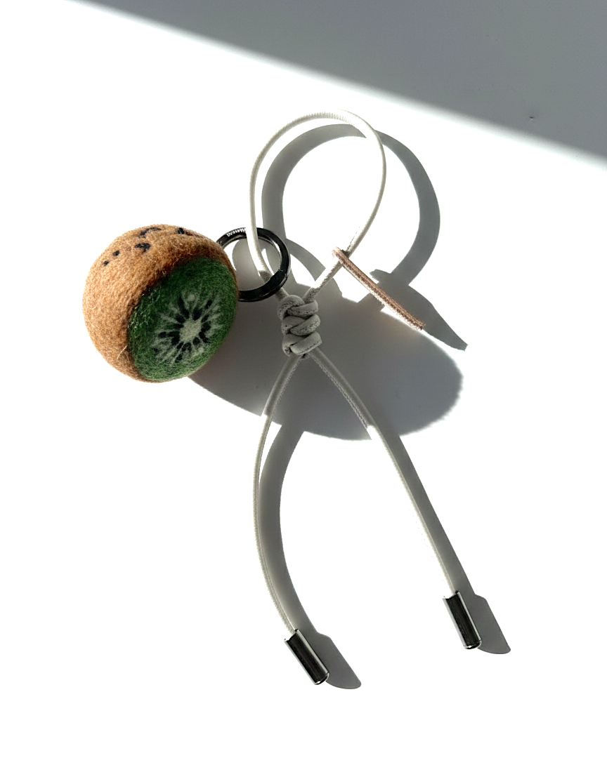 Handcrafted needle-felted kiwi plush charm with an off-white cream cord on a white background.